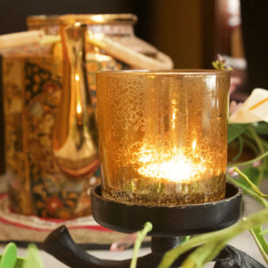 A glowing candle in a glass holder with decorative background.